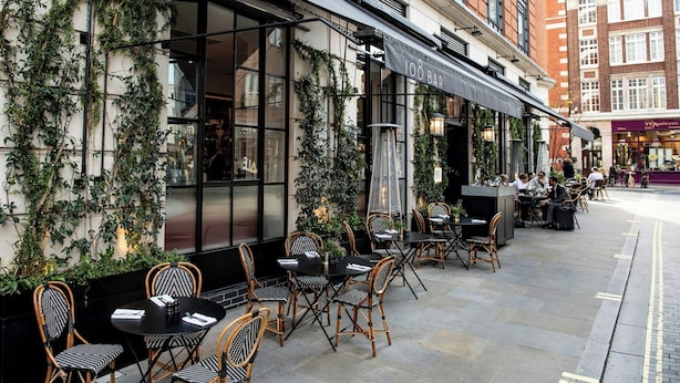 An outdoor seating area with tables and chairs, a bar, and a building facade with greenery. - Relaxing Studio Double Bed At Marylebone (London)