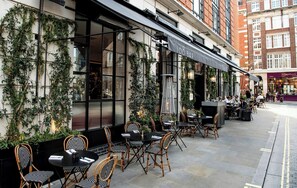 An outdoor seating area with tables and chairs, a bar, and a building facade with greenery. - Relaxing Studio Double Bed At Marylebone (London)