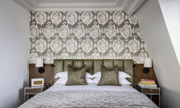 A neatly arranged bedroom with a patterned wallpaper, a tufted bedspread, and two bedside tables with lamps and books. - Relaxing Studio Double Bed At Marylebone (London)