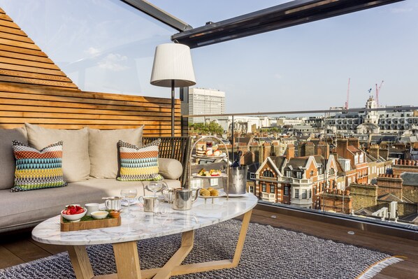 A rooftop terrace with a sofa, table, and city view. - Relaxing Studio Double Bed At Marylebone (London)