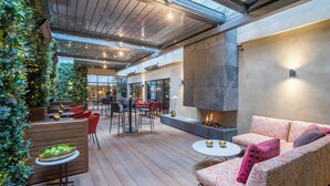 An indoor-outdoor lounge area with a fire feature, seating, and a glass wall. - Relaxing Studio Double Bed At Marylebone (London)