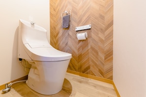 A modern toilet with a control panel, a towel rack, and a toilet paper holder on a wooden herringbone floor. - Mt. Fuji Resort Club-ZEN- (Fujikawaguchiko)