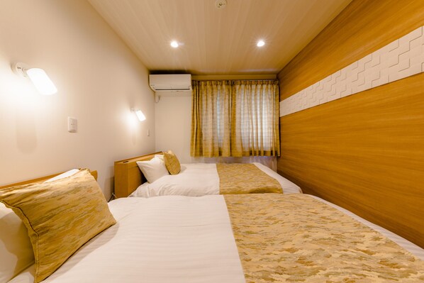 Habitación de hotel con dos camas, cabecero de madera, ventana con cortinas y un equipo de aire acondicionado en la pared.