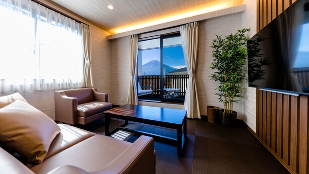 A modern hotel room with a sofa, a coffee table, a TV, and a balcony with a mountain view. - Mt. Fuji Resort Club-RIN- (Fujikawaguchiko)