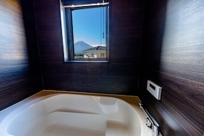 A modern bathroom with a large bathtub, a window with a view of a house and a mountain, and a control panel on the wall. - Mt. Fuji Resort Club-RIN- (Fujikawaguchiko)