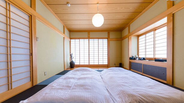 Ett traditionellt japanskt rum med tatamimattor på golvet, en futonmadrass, skjutdörrar och en utsikt genom ett fönster med träram.