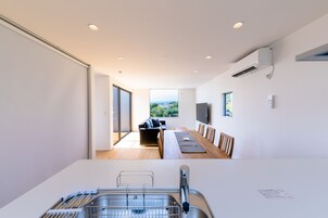 Una cocina moderna con lavavajillas integrado, un comedor con una mesa larga y sillas, y un amplio ventanal con vistas al exterior.