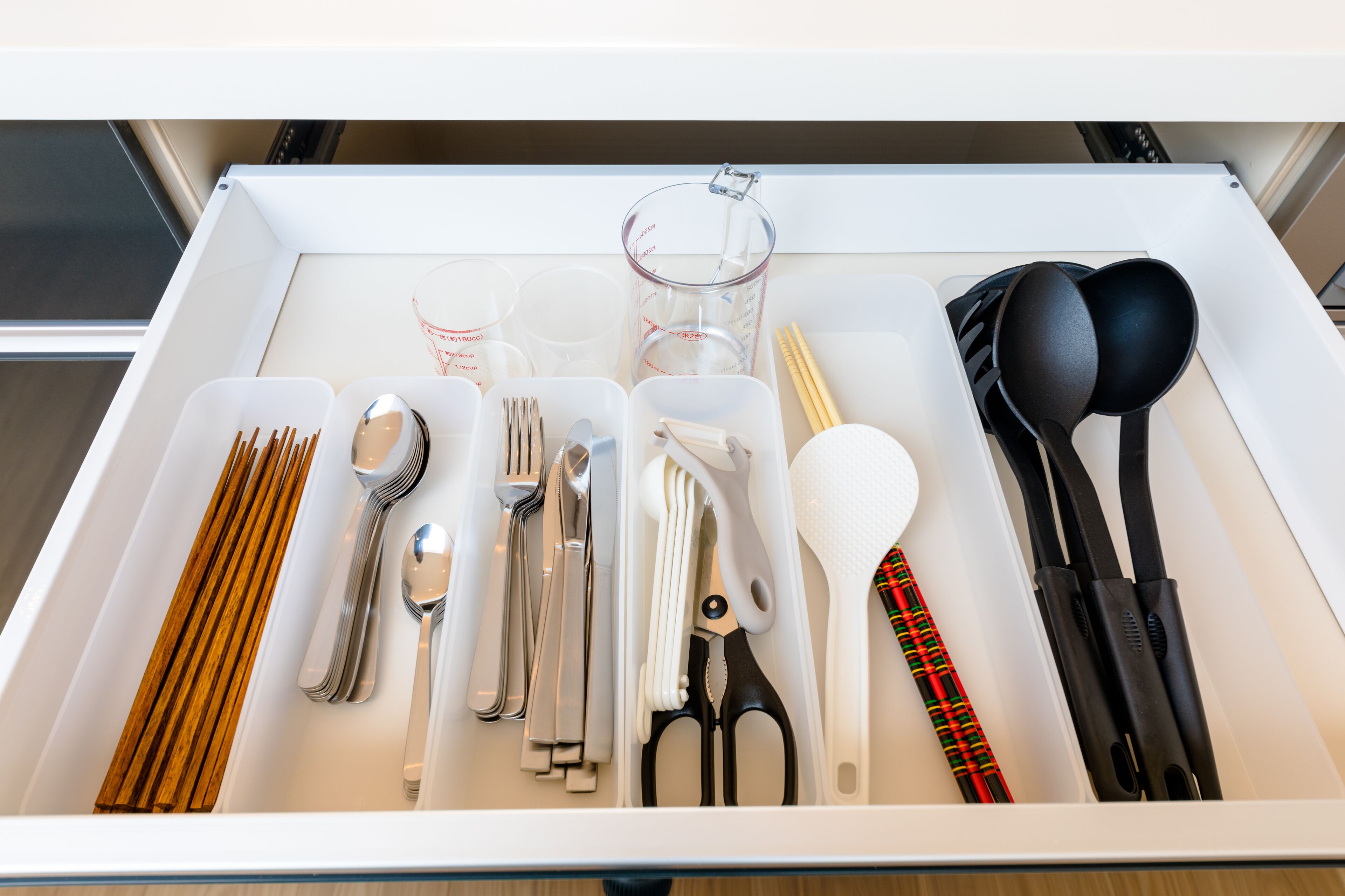 A drawer with neatly organized kitchen utensils including spoons, forks, knives, and measuring cups.