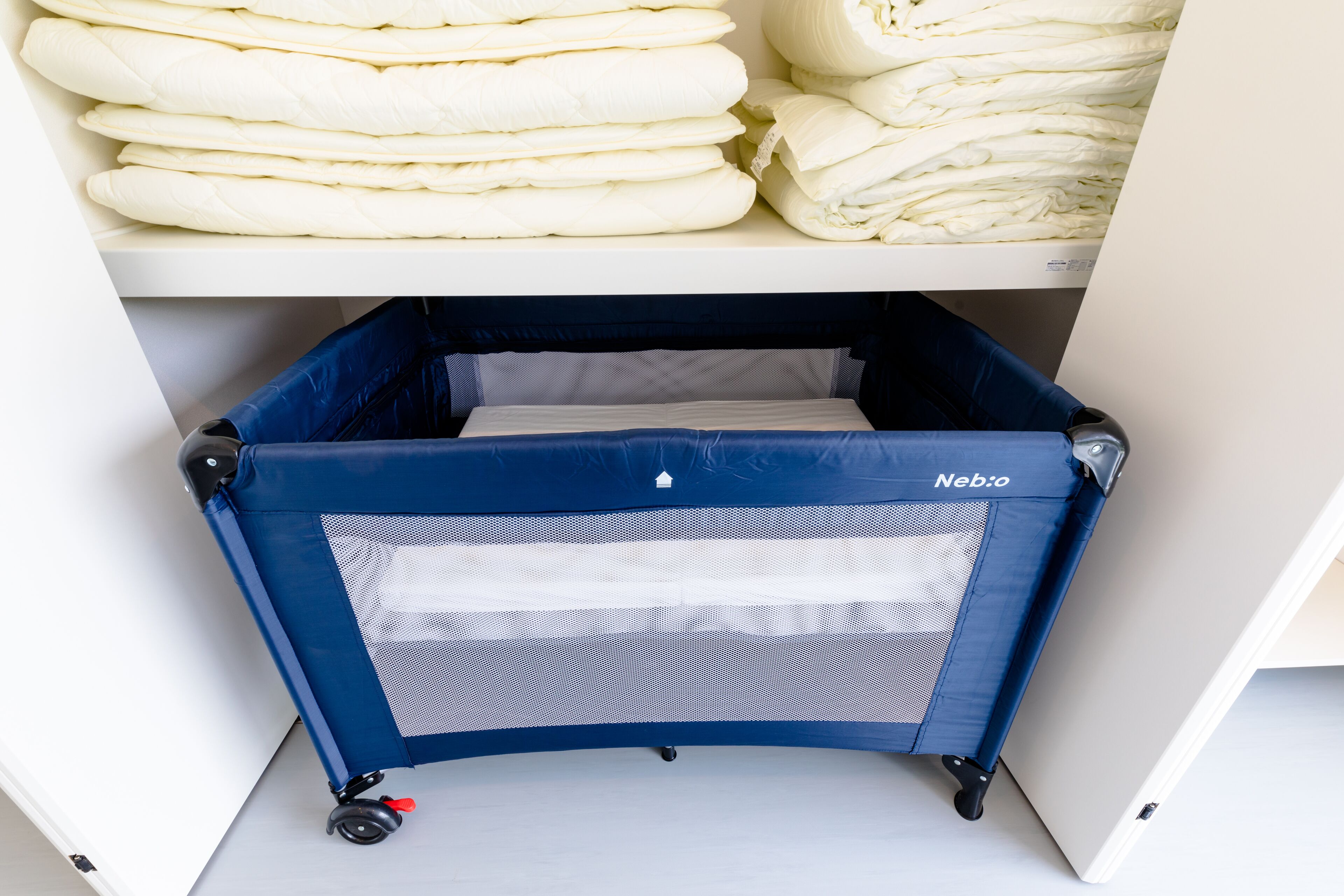 A storage area with neatly stacked bedding and a blue baby stroller with wheels.