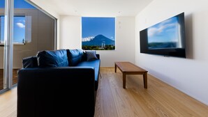 A modern living room with a large window, a flat-screen TV, a wooden coffee table, and a blue sofa. - Frame View Mt.Fuji Villa West (Fujikawaguchiko)
