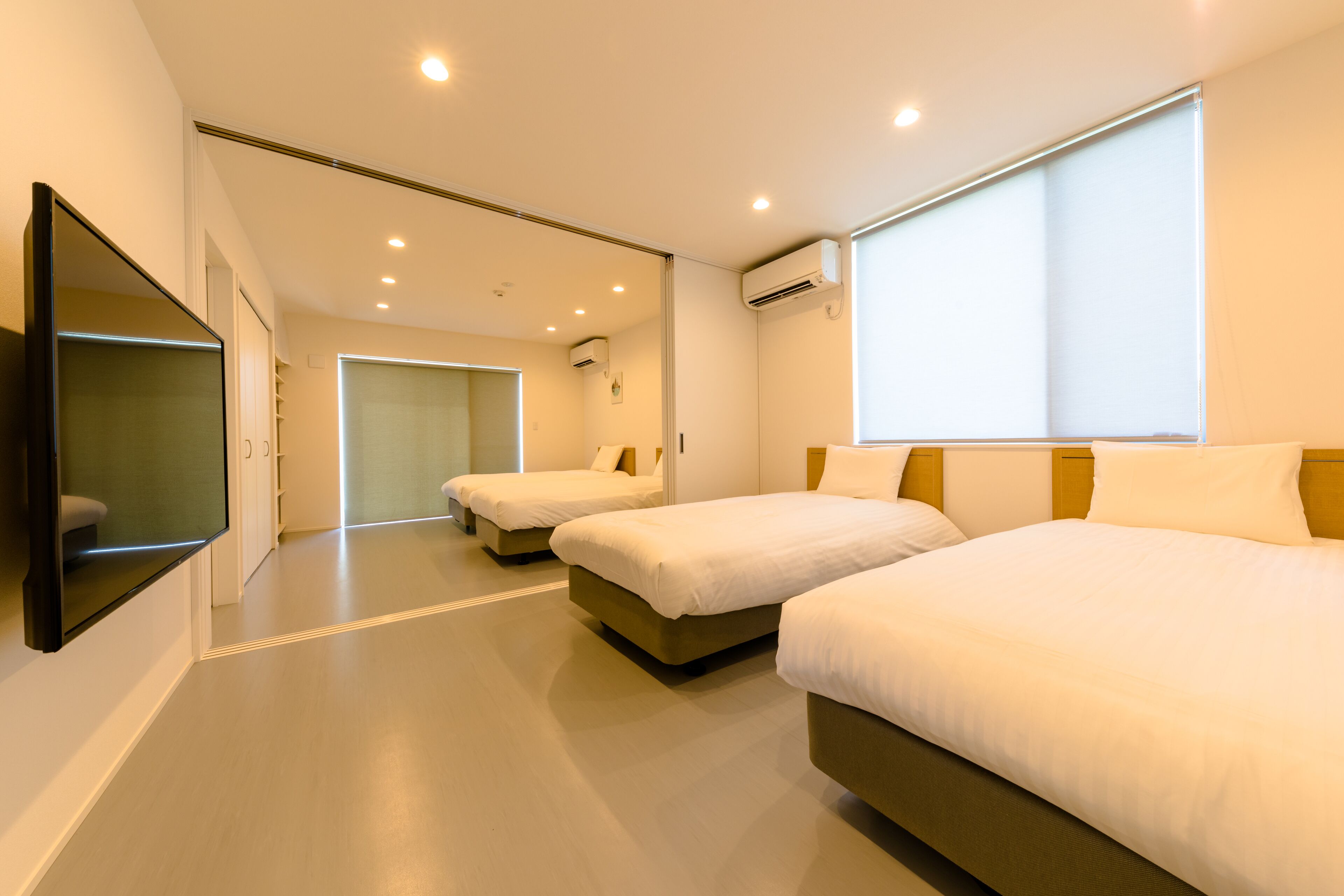 A hotel room with two beds, a flat-screen TV mounted on the wall, and a large window providing natural light.