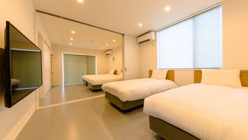 A hotel room with two beds, a flat-screen TV mounted on the wall, and a large window providing natural light.
