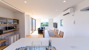 A modern kitchen with a built-in dishwasher, a large window, and a dining area with a view. - Frame View Mt.Fuji Villa West (Fujikawaguchiko)