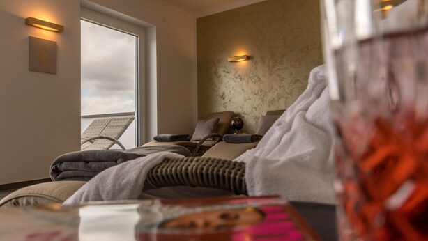 Een moderne hotelkamer met een groot raam, een bed met uitzicht, een massagestoel en een wandlamp.