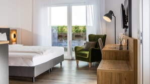 Een moderne slaapkamer met een bed, een groene fauteuil, een bureau en een televisie.