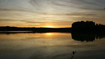 A calm lake at sunset with a silhouette of trees on the right.