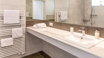 A modern bathroom with a large mirror, two sinks, and a towel rack with multiple towels.