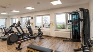 Een sportschool met diverse fitnessapparaten, grote ramen en uitzicht op de omgeving.