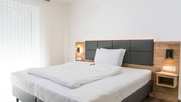 Ein modernes Hotelzimmer mit einem großen Bett, einem hölzernen Kopfteil, Nachttischlampen und einem kleinen Nachttisch.