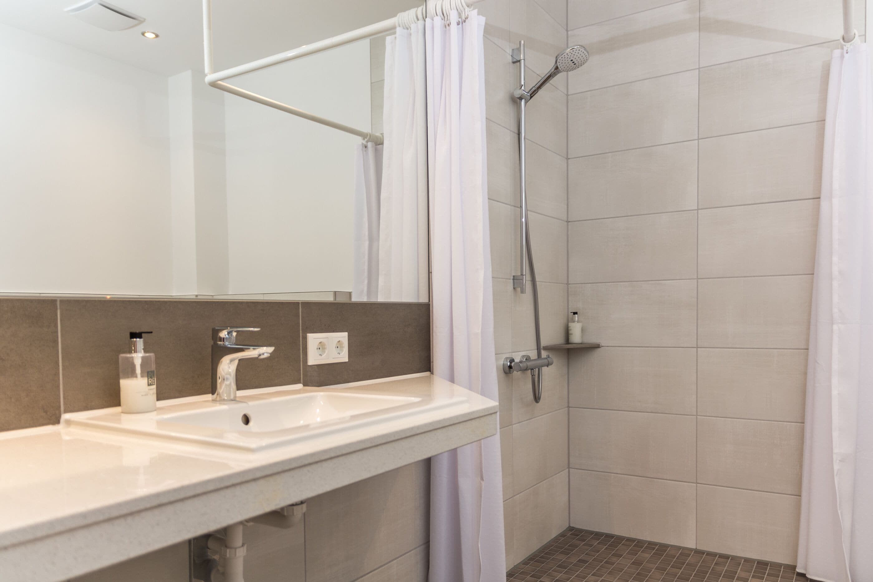 Une salle de bain moderne avec un lavabo blanc, un miroir et une douche.