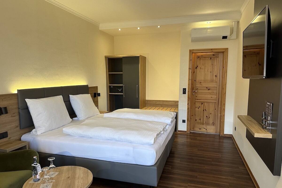 Een moderne hotelkamer met een groot bed, een klein rond tafeltje, een kledingkast en een aan de muur bevestigde televisie.
