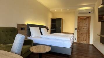 A hotel room with a bed, a green armchair, a small round table, and a wooden wardrobe.