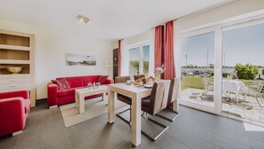 Un salon moderne avec un canapé rouge, une table à manger avec des chaises et une vue sur l’extérieur grâce à de grandes portes-fenêtres coulissantes.