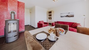 Un salon moderne avec une cheminée, des canapés rouges, une table à manger dressée avec des assiettes et des tasses, et une bibliothèque.