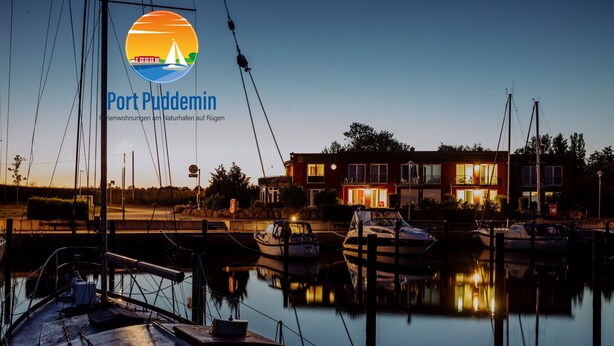 Un port de plaisance au crépuscule, avec des bateaux amarrés, un bâtiment rouge illuminé et un logo représentant un voilier.