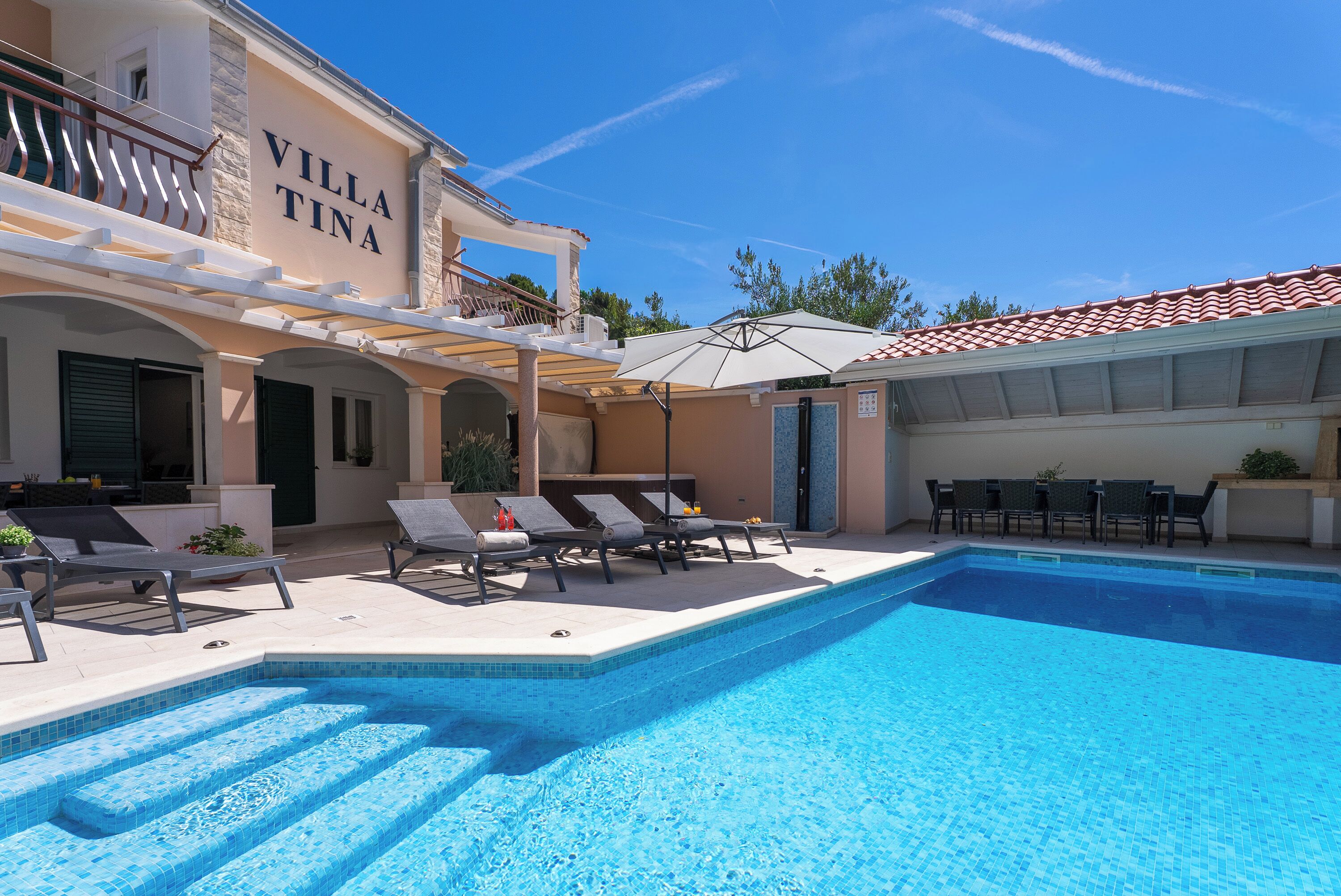 Un espace piscine avec des chaises longues et un bâtiment portant l’inscription « VILLA TINA ».