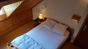 Ein Einzelbett mit weißer Bettwäsche in einem Zimmer mit Holzbalkendecke und einem kleinen Nachttisch mit Lampe.