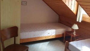 Una cabaña pequeña de una sola habitación con techo inclinado, una silla de madera, dos camas individuales y una mesita con una lámpara.