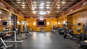 Un gimnasio con diversos equipos de ejercicio, una pantalla de televisión y paneles de madera en las paredes.