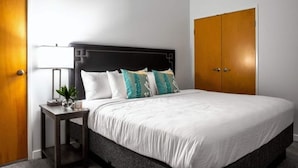 Una habitación de hotel con una cama grande, una mesita de noche con lámpara y un armario.
