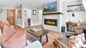 A modern living room with a fireplace, a mounted TV, and a cozy seating area. - Luxury five bedroom condo, outdoor swimming pool, walk to hiking and biking trails (Park City)