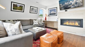 A modern living room with a grey sofa, a fireplace, and framed pictures on the walls. - Walk to Skiing, Stunning Top Floor Condo at Park City Base, Professionally Decorated Luxury 3BR (Park City)