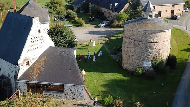 Ein ländliches Anwesen mit Steingebäuden, einem großen zylindrischen Turm und einer Rasenfläche mit Menschen.