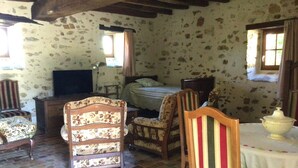 Ein rustikaler Raum mit Steinwand, einem Bett, einem Fernseher und einem Esstisch mit weißem Tischlein.