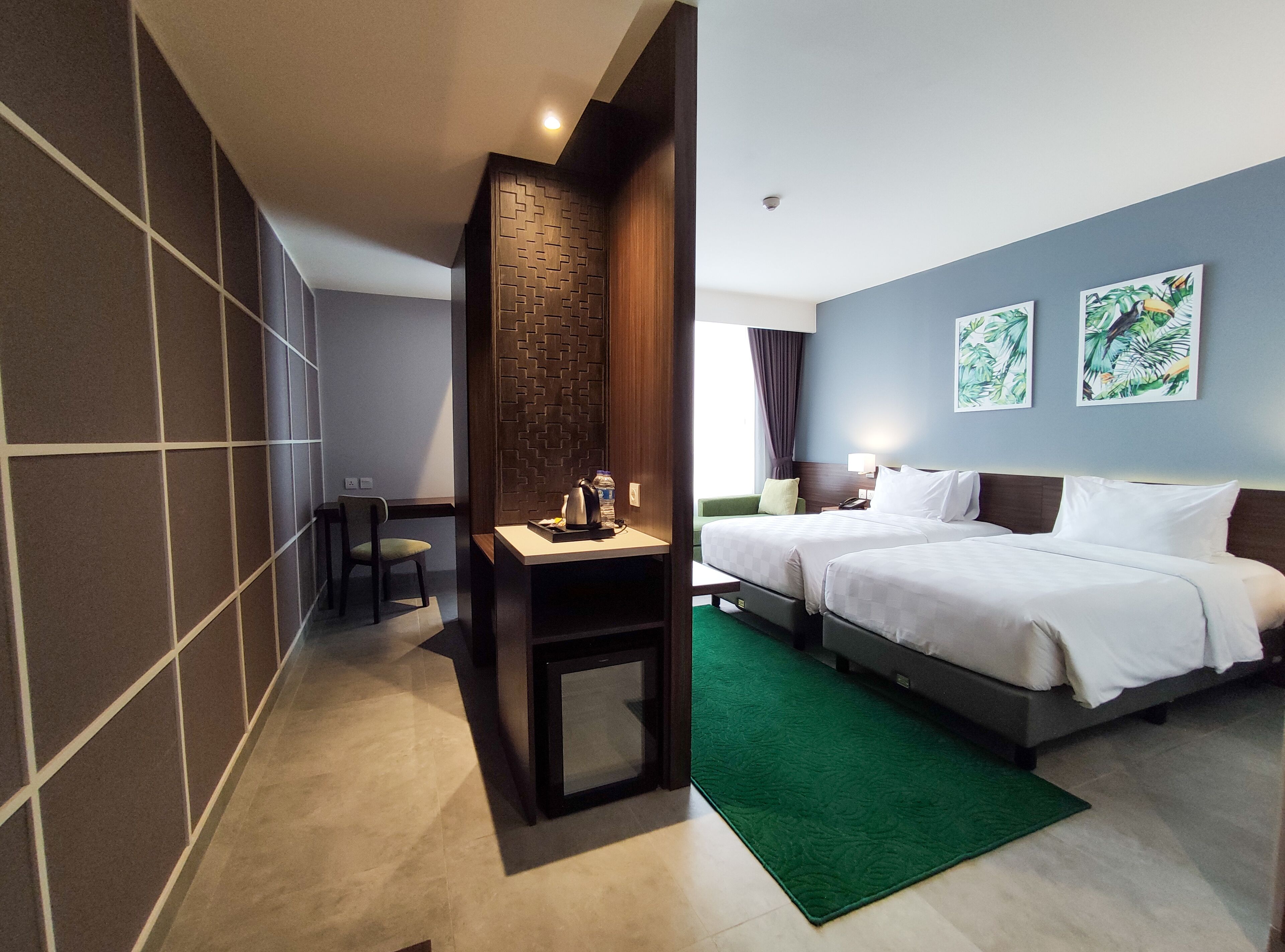 A hotel room with two beds, a desk with a kettle, a chair, and a green rug.