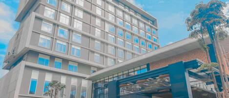 A multi-story hotel with a modern architectural design, featuring a prominent entrance with a glass canopy and a landscaped garden area.