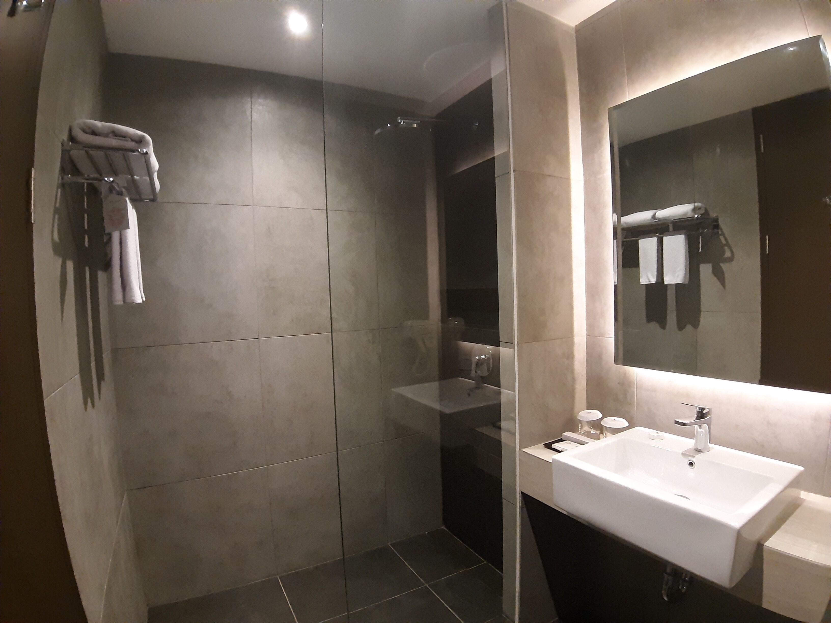 Een moderne badkamer met een douchecabine van glas, een witte wastafel en een grote spiegel.