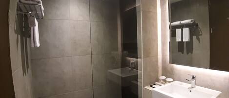 Een moderne badkamer met een douchecabine van glas, een witte wastafel en een grote spiegel.
