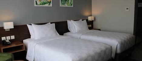 Habitación de hotel con dos camas, una mesita pequeña y dos lámparas fijadas a la pared.