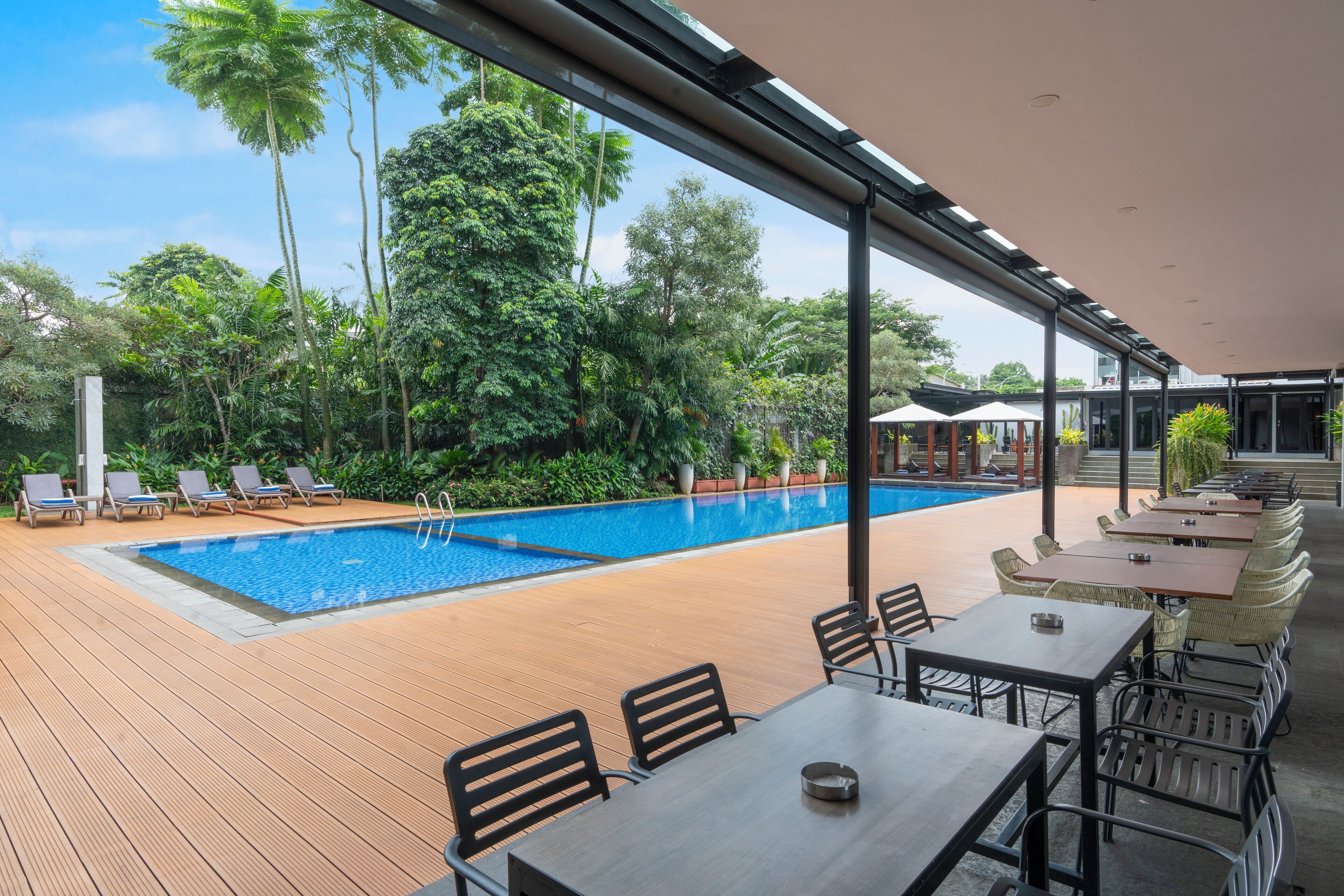 Un espace aménagé au bord de la piscine, avec une terrasse en bois, des chaises longues et des tables.