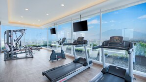 Un gimnasio moderno con cintas de correr, elípticas y máquinas de pesas, con amplias ventanas y vista a la ciudad.