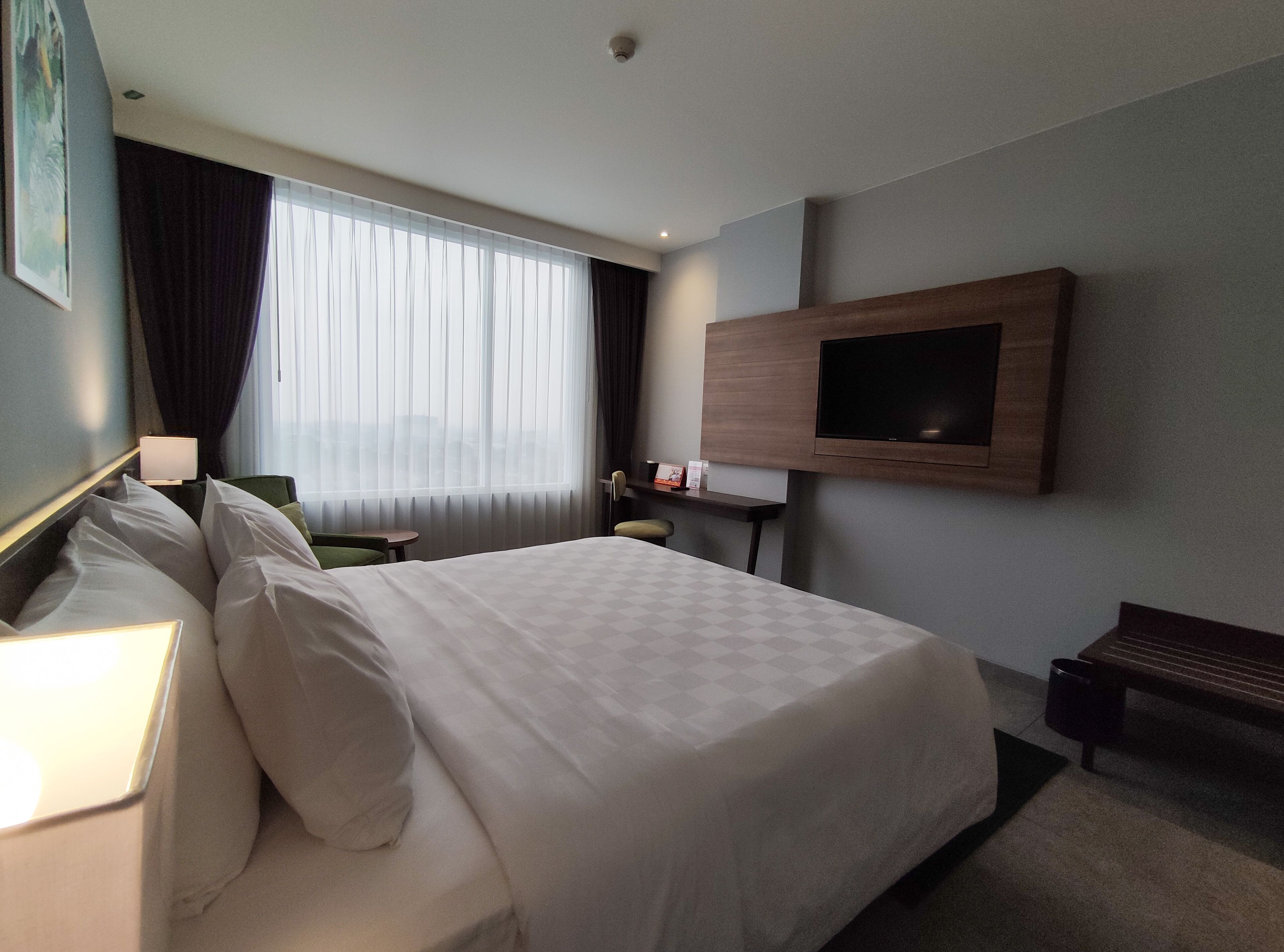 A hotel room with a large bed, a TV mounted on the wall, a small table, and a chair.