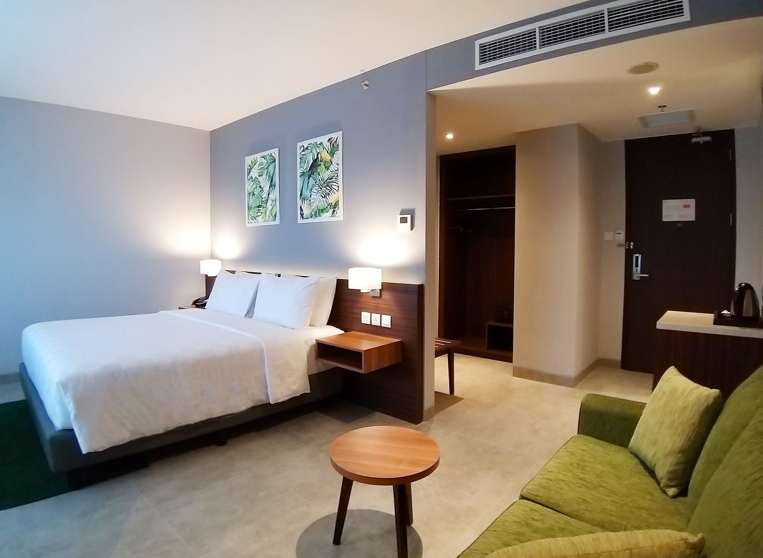 Et hotelværelse med en seng, et natbord, en lampe, en grøn sofa og et lille rundt bord.