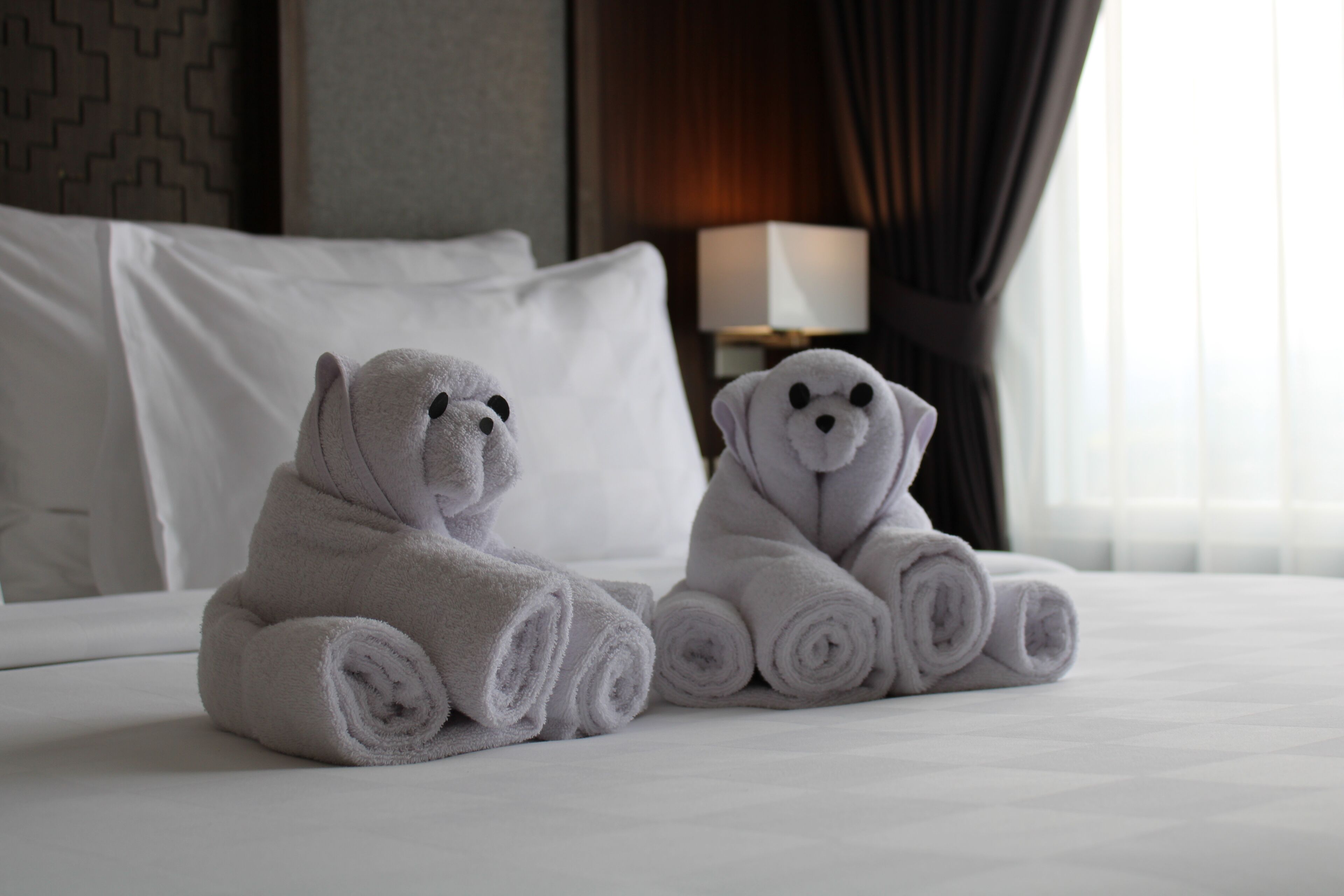 Zwei zusammengerollte Handtücher in Bärenform auf einem Bett in einem Hotelzimmer.