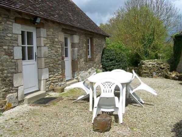 Un bâtiment en pierre avec une allée en gravier et un ensemble de table et de chaises en plastique blanc.