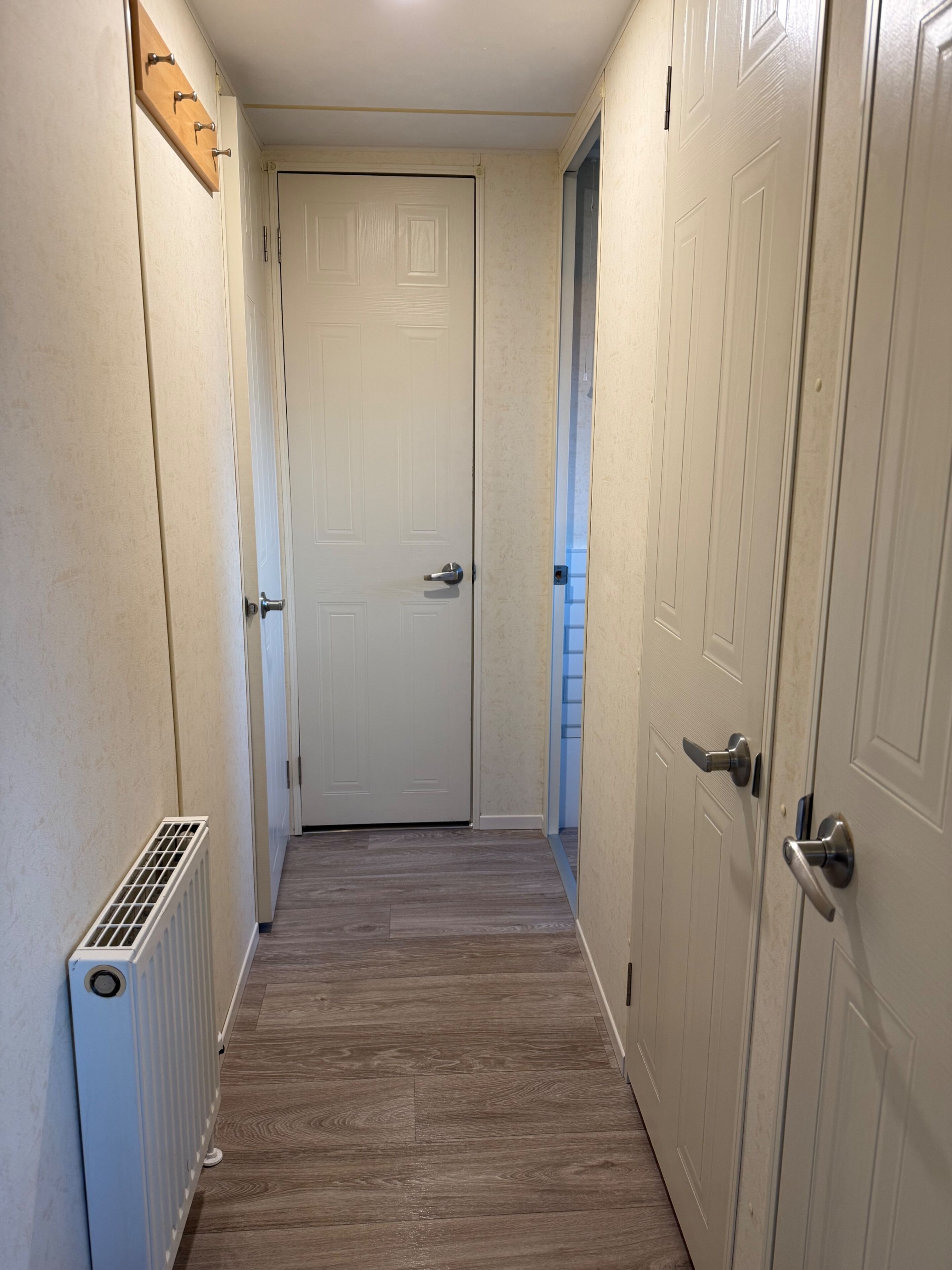 Un couloir étroit avec un plancher en bois, des portes blanches et un radiateur sur le côté gauche.